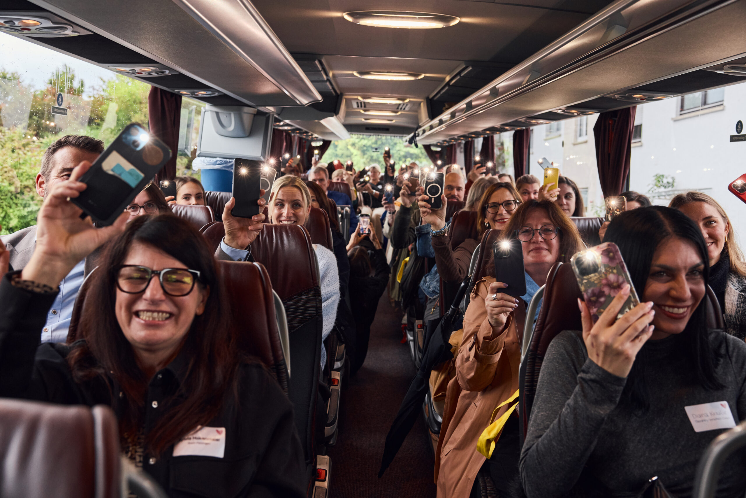 Gruppe von Reisenden sitzt in einem Reisebus und h&auml;lt ihre Smartphones mit eingeschaltetem Licht in die H&ouml;he.